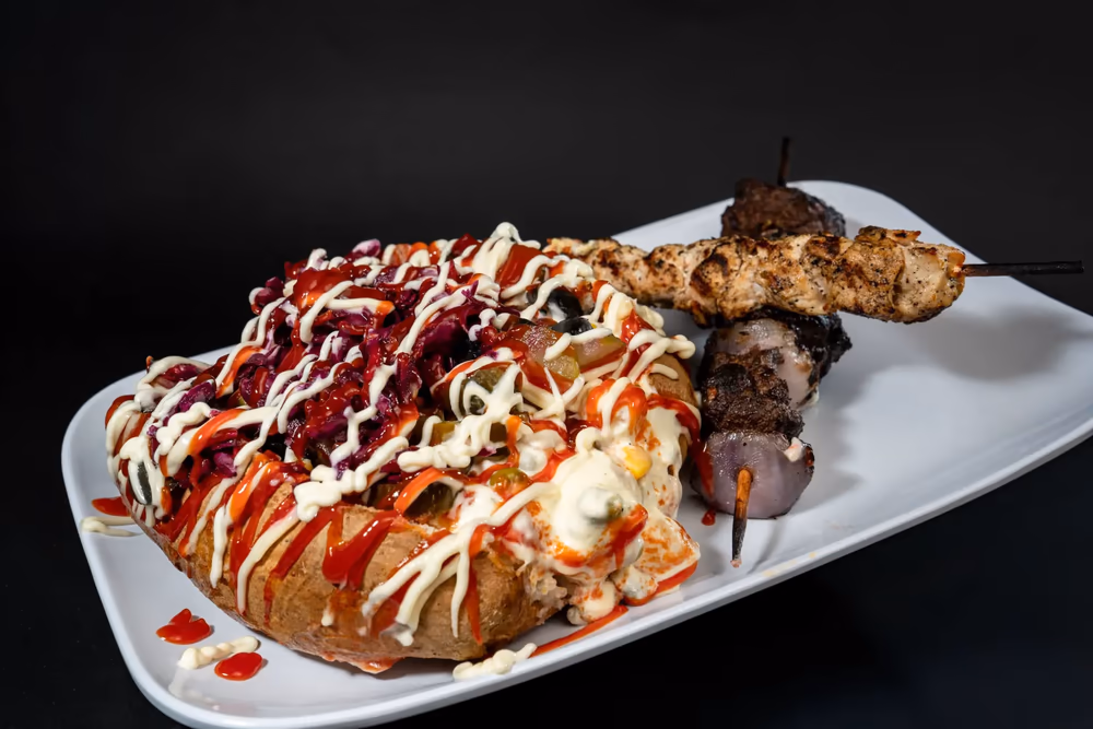 A loaded Turkish kumpir served alongside kebab skewers at FRIES B4 GUYS in Allston, Boston