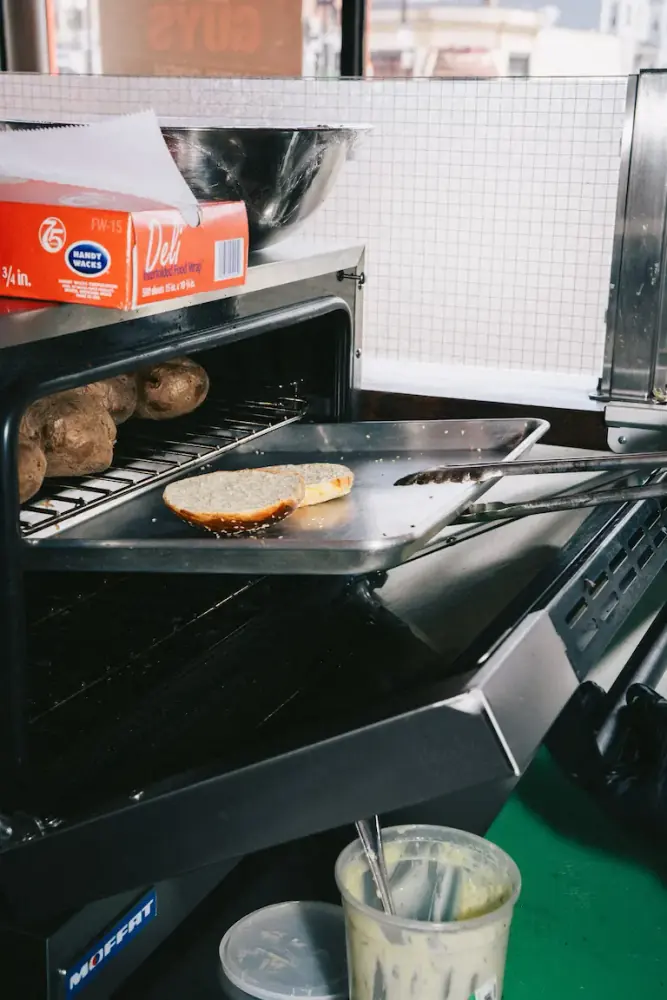 Turkish kumpir oven with potatoes baking on the top rack and a burger bun toasting on the lower tray